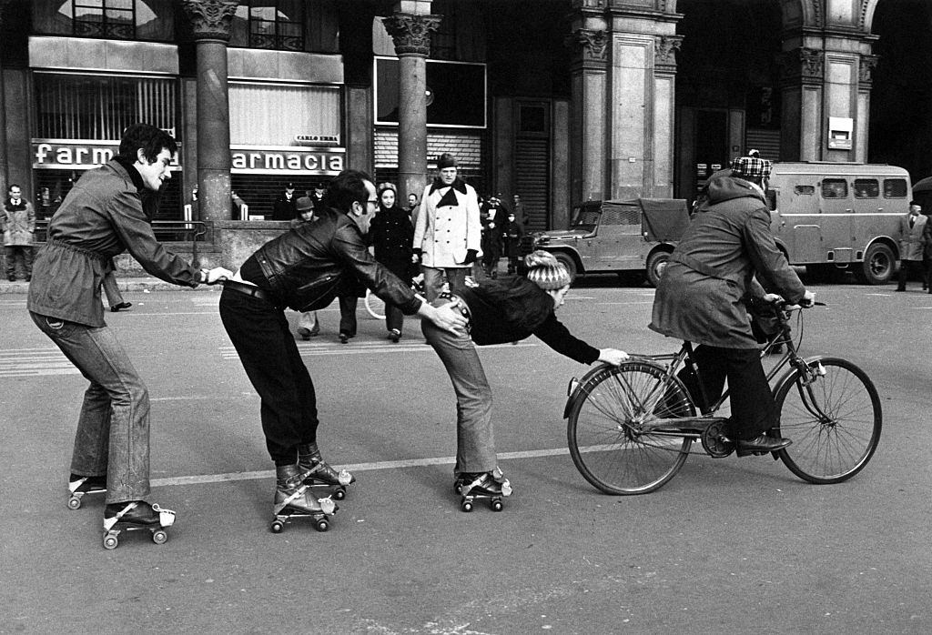 #13 A man in bicycle drawing a little girl and two boys in roller skates on Piazza del Duomo during the first Italian walking sunday due to the oil crisis, 1973.