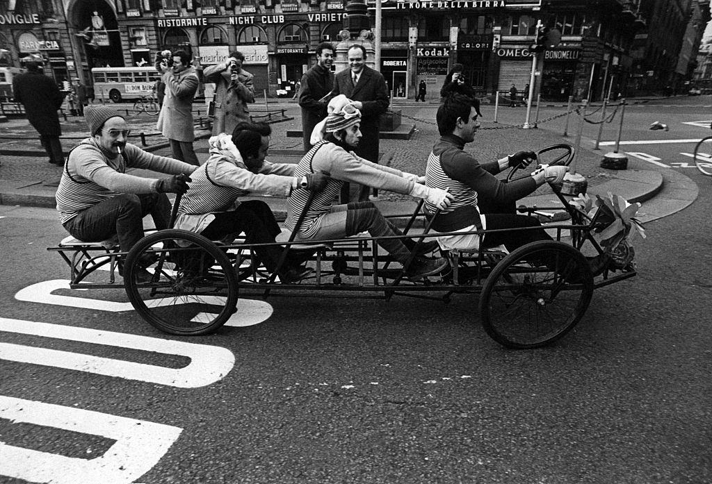 #30 Four men on a tandem bicycle crossing Piazza del Duomo during the first Italian walking sunday due to the oil crisis. Milan, 2nd December 1973