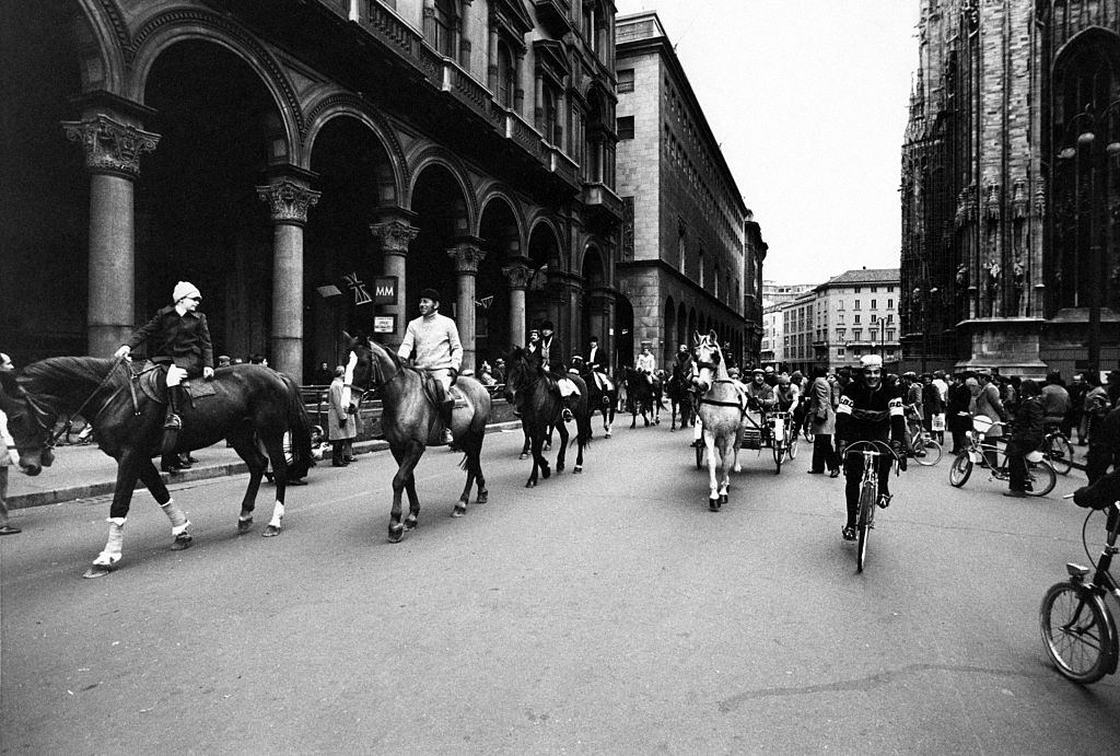 #31 Some people riding horses, gigs and bicycles across Piazza del Duomo during the first Italian walking sunday due to the oil crisis.