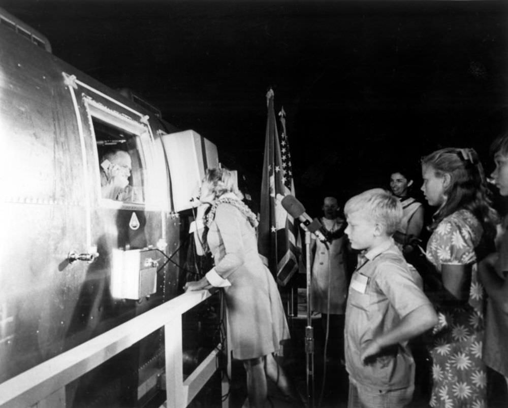#8 Joan Aldrin speaks on the phone to her husband, Buzz, while he gazes out from the Apollo 11 Mobile Quarantine Facility aboard the U.S.S.