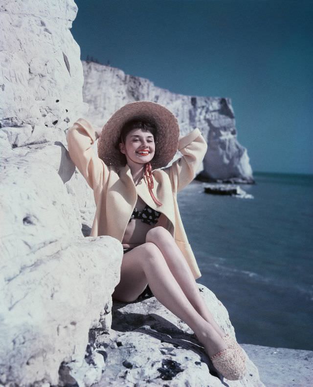 #9 Audrey Hepburn sitting on a rock wearing a hat and beachwear, 1951.