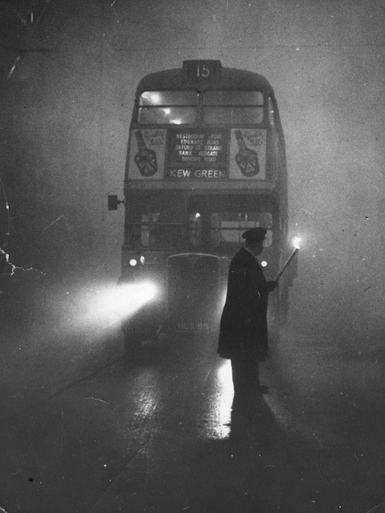 #23 A man guiding a London bus through thick fog with a flaming torch.