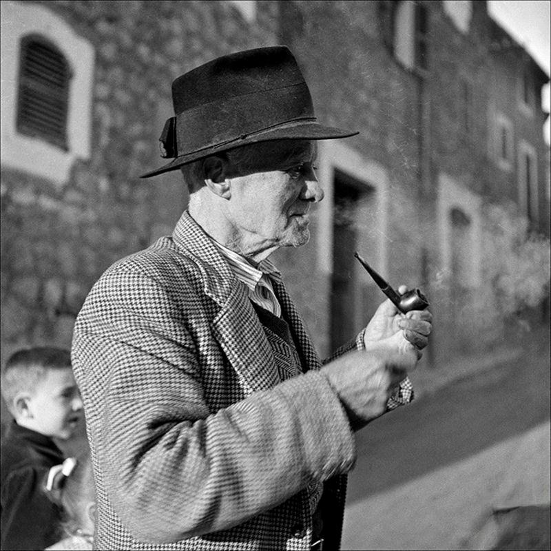 #33 An old man smoking in the street and children in the background, 1956
