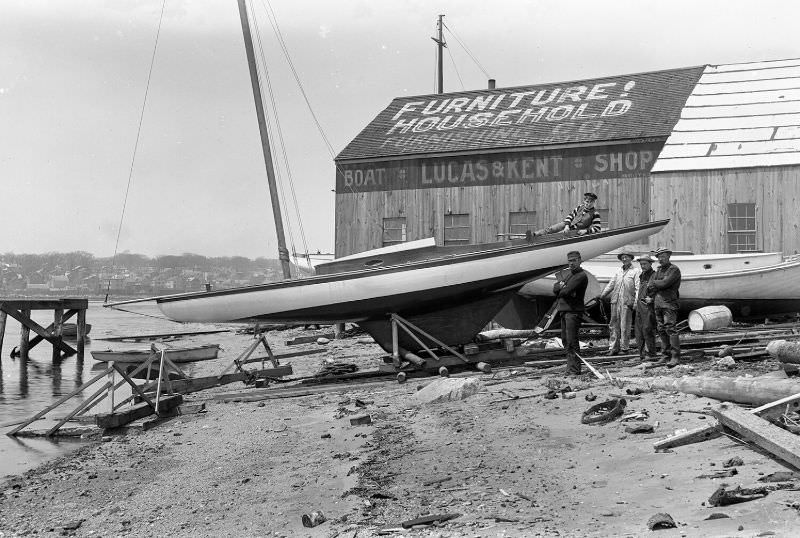 #24 Men posed around sailboat. Lucas & Kent Boat Shop in the background, 1907
