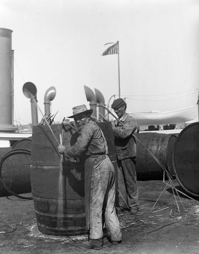 #19 Coopers at work on oil barrels “flagging” a cask, New Bedford, 1918