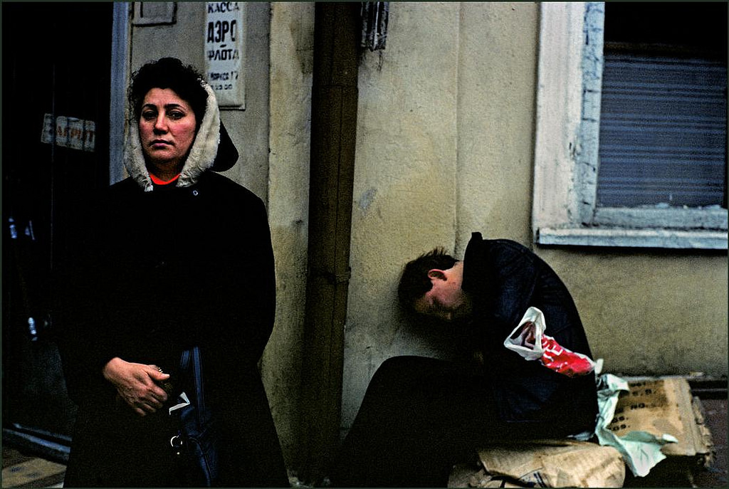 #16 A woman waiting on the street ignores a drunk seemingly comatose behind her.