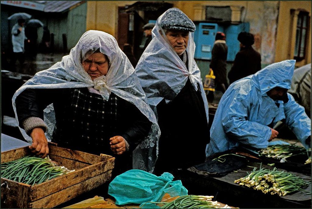 #2 Men and women market stall holders shelter from heavy rain under plastic sheeting whilst sorting their onions.