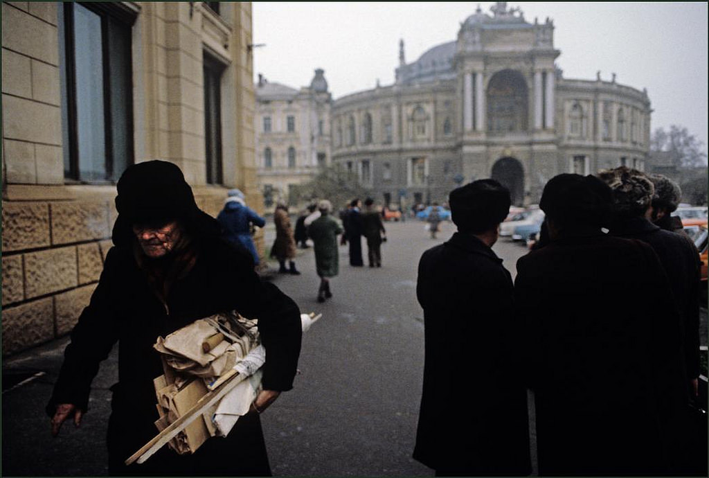 #21 Old man with his bundle of wood and cardboard hurries along in the cold with the Opera Theatre in the background.