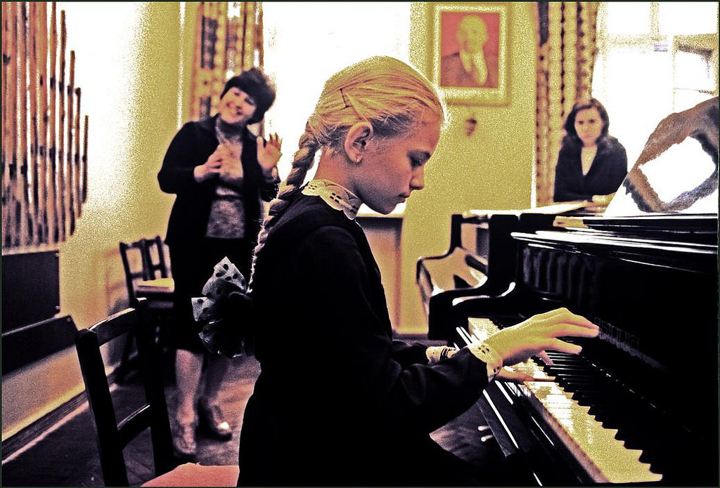 #27 A young girl playing the piano under instruction at the famous Stolyarsky Music School with a portrait of Lenin on the wall.