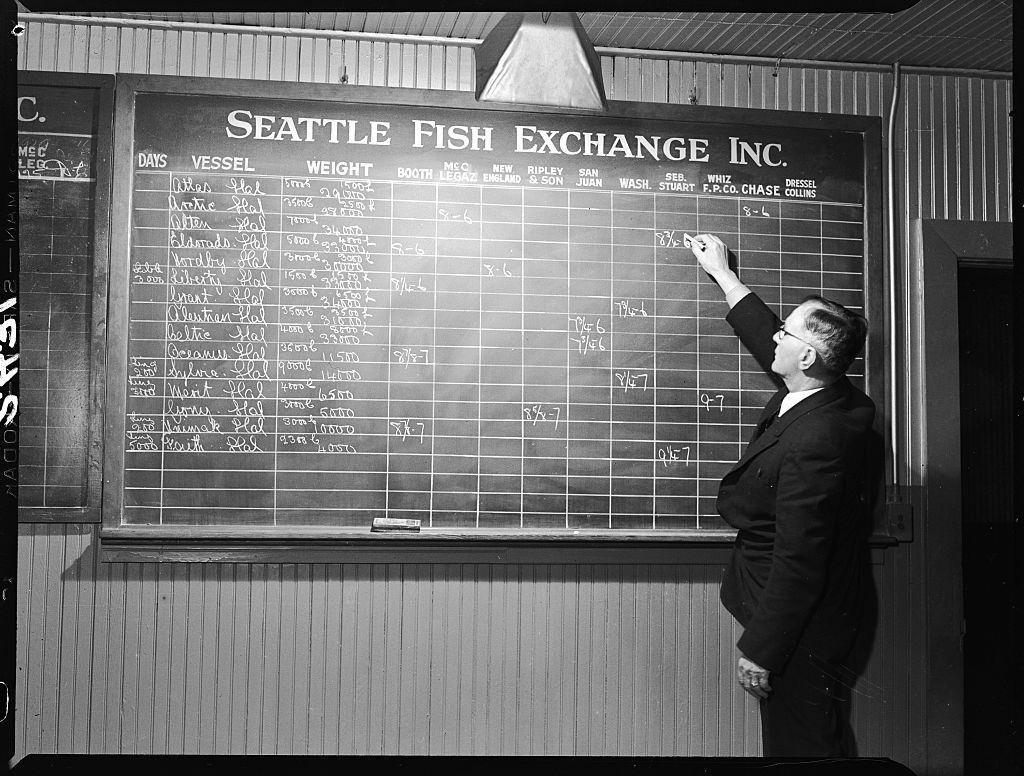 #22 Bill Maddock tracks fish for sale on a blackboard at the Seattle Fish Exchange.