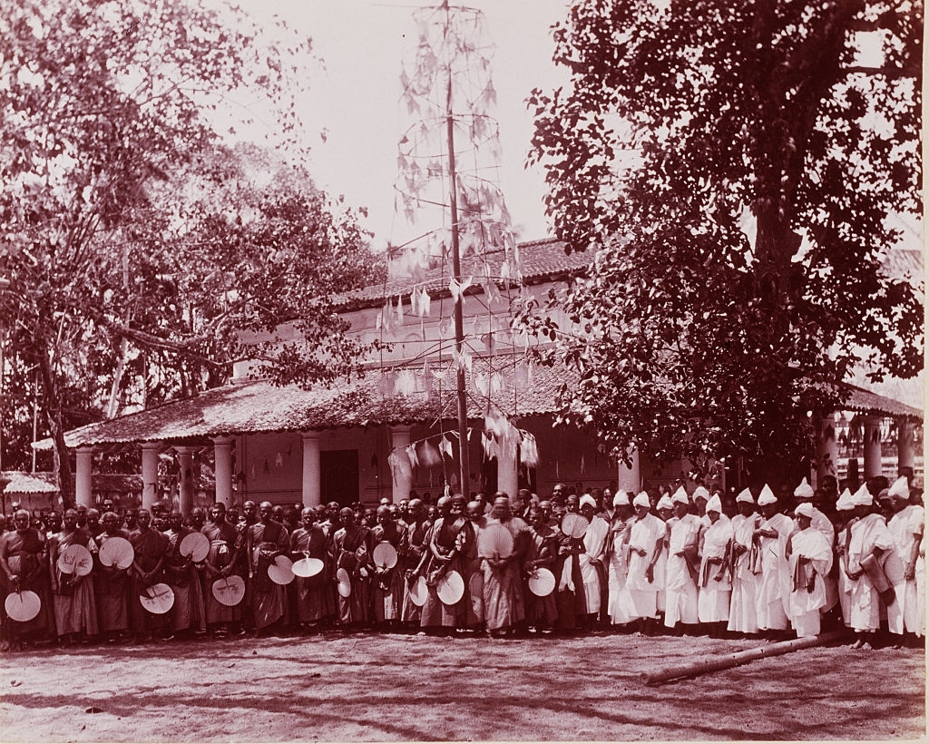 #42 A group of men dressed in white robes standing next to another group of men, several of whom carry straw fans, Sri Lanka, 1880s.