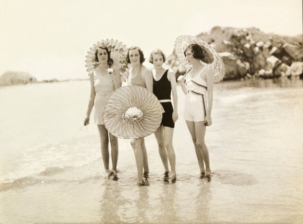 #24 Mrs. Douglas, Mrs. Cushing, Mrs. Phipps, and Mrs. Stevens holding parasols and standing with their feet in water at the beach, in Newport, Rhode Island.