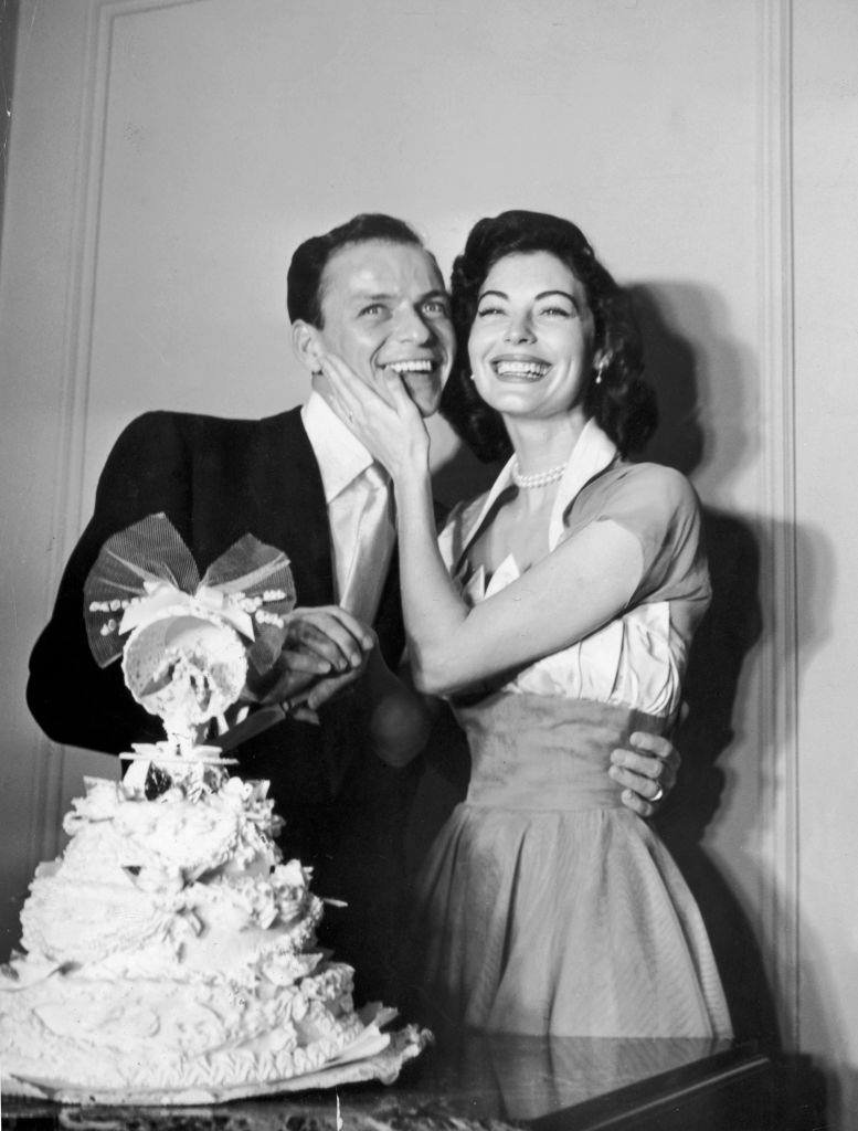 #20 Frank Sinatra and Ava Gardner standing behind their wedding cake on their wedding day.