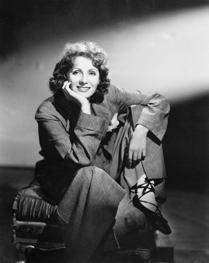 #6 Greta Garbo seated on an ottoman, wearing a large business suit and sporting ballet shoes, 1930s.