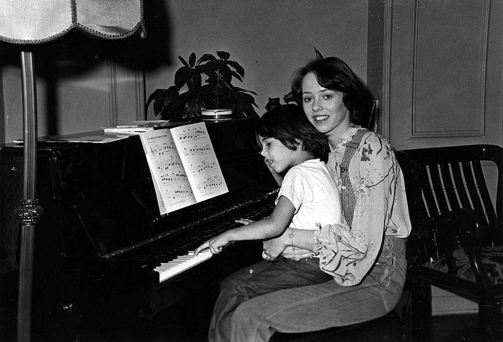 #6 Mackenzie Phillips with a baby at the piano on December 3, 1976