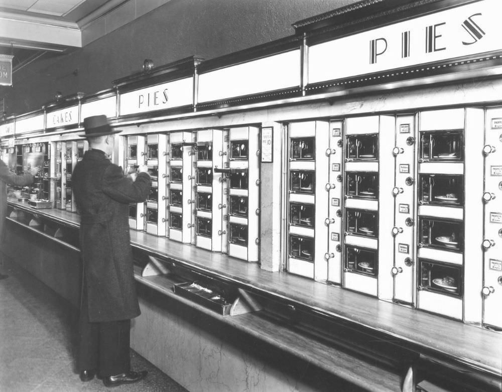 #1 Automat, 977 Eighth Avenue, Manhattan. Man takes pie out of Automat, stone counters and walls below metal and glass display.