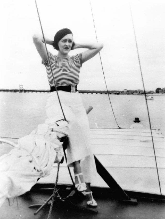 #17 A woman is posed sitting on the boom of a sailing vessel, Queensland