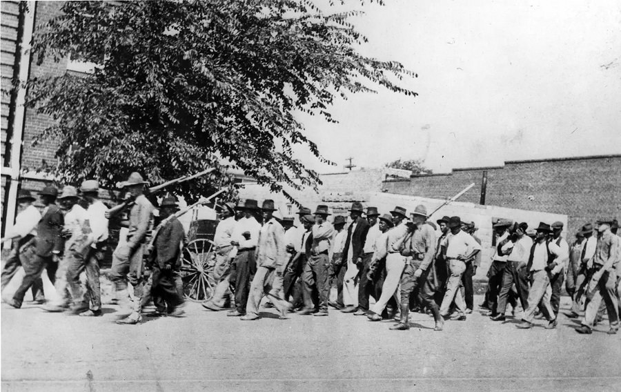 #6 A group of National Guard troops, carrying rifles with bayonets attached, escort unarmed Black men to the detention center at the Tulsa convention hall in June 1921.