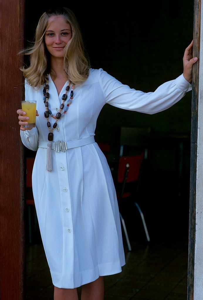 #4 Cybill Shepherd holding a glass of orange juice, wearing a white dress with a pleated skirt, Glamour 1970.
