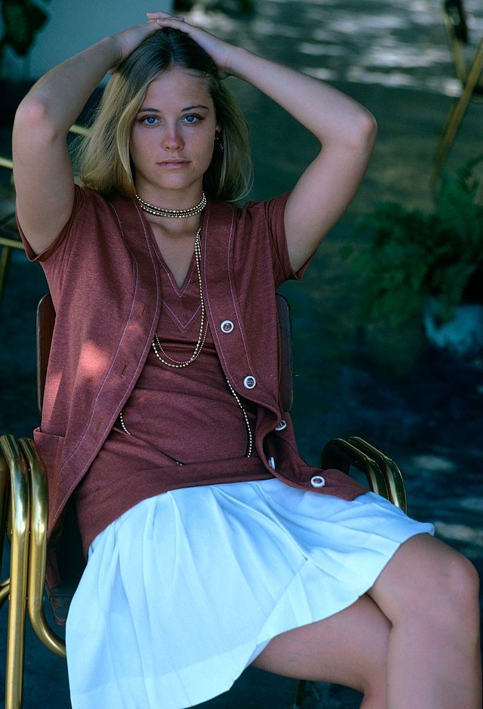 #5 Cybill Shepherd sitting in chair wearing amber, white stitched jacket, Glamour 1970.