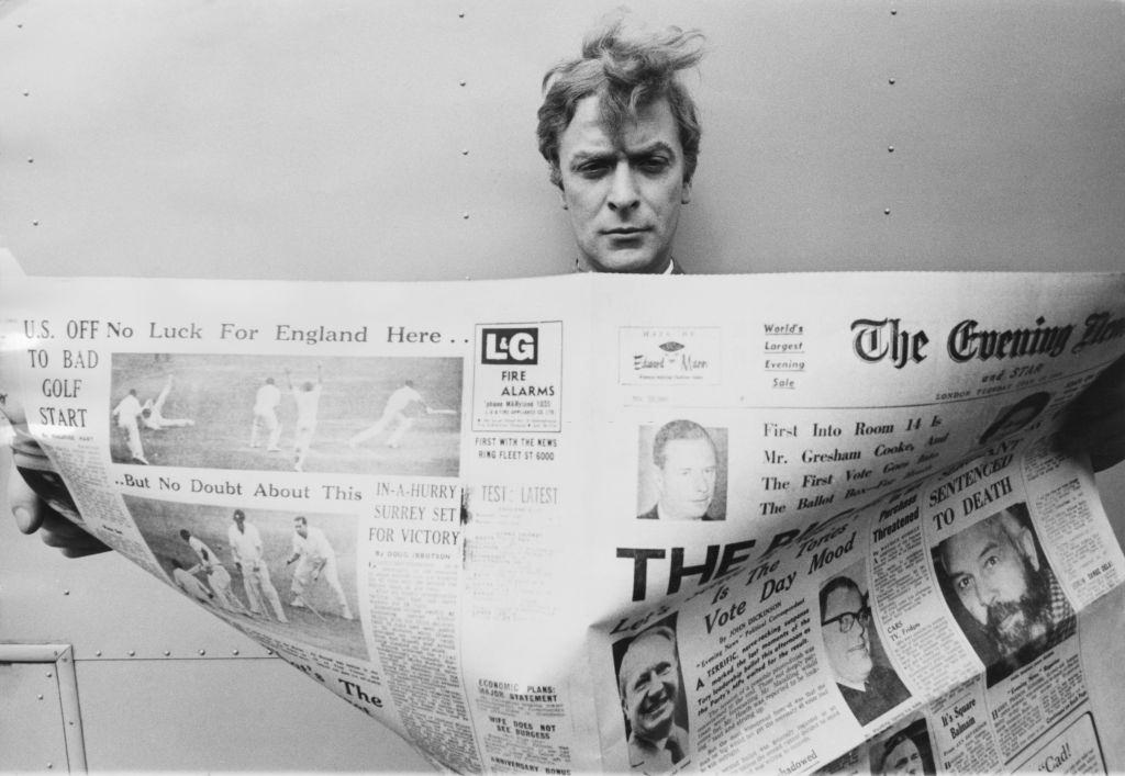 #37 Michael Caine reading a copy of the Evening News, 1960s.