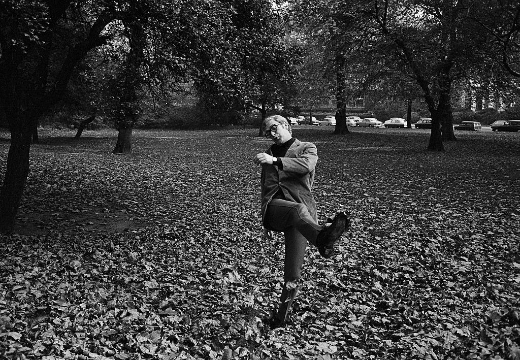 #43 Michael Caine kicks, in a London park covered with fallen leaves, 1965.