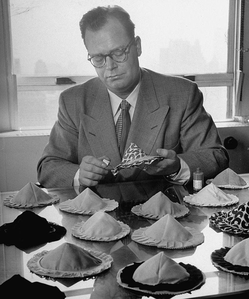 #1 Inventor of Poses, Charles L. Langs sitting at his desk full of his inventions, strapless, backless, wireless bras.