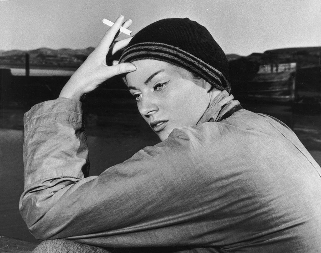 #32 Anita Ekberg, dressed in costume, looks over her shoulder while smoking a cigarette, 1955.