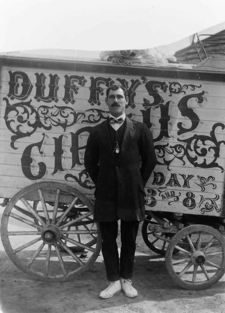 #25 Duffy’s Circus, man standing in front of a wagon labelled, ‘Duffy’s Circus’, 1911.