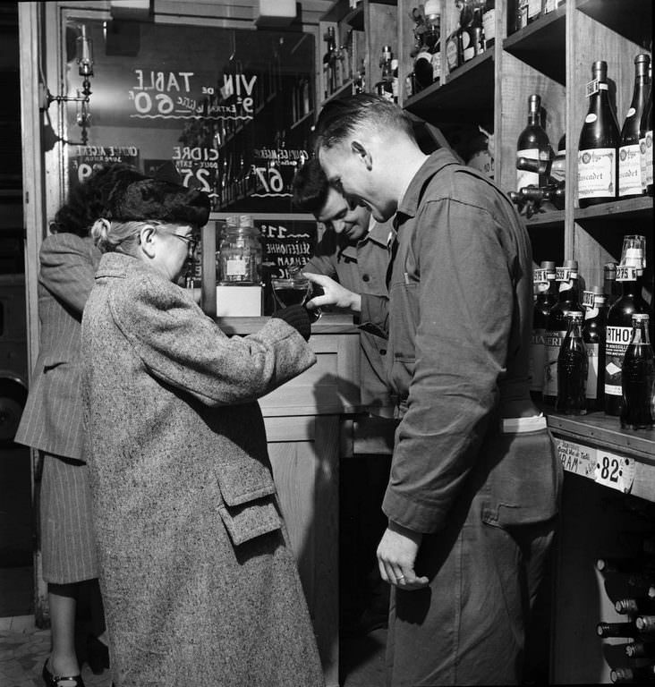 #11 In a Paris shop, a man pours a bottle of Coca-Cola into a glass held by an elderly woman.