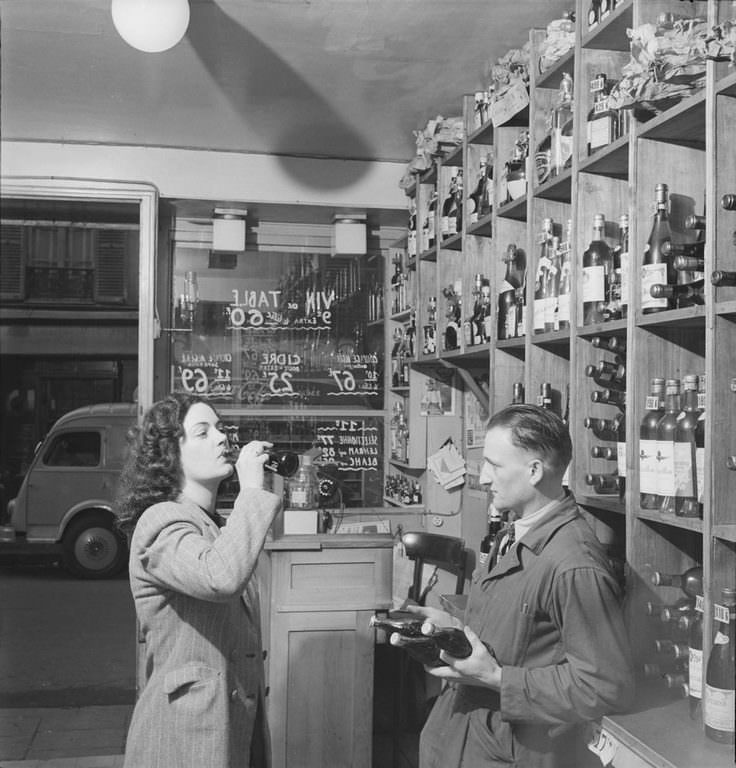 #2 Watched by a man with several bottles in his hands, a woman drinks a bottle of Coca-Cola in a shop, in Paris, France.