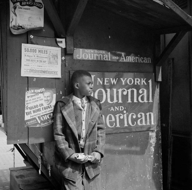 #15 A newsboy standing by his newsstand holding a magazine, 1943.