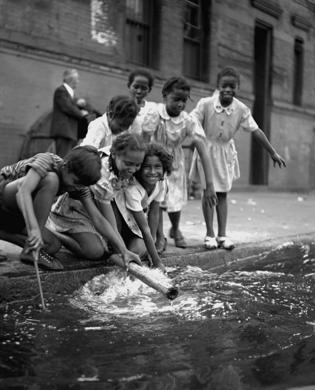 #25 Young girls play beside a flooded street drain, 1947.