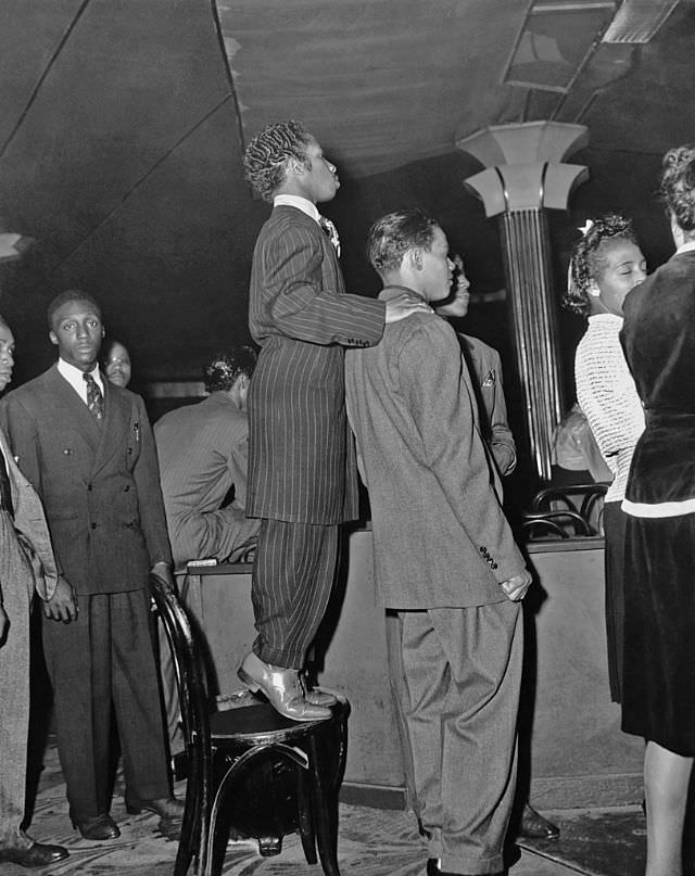 #3 A short man, wearing a zoot suit, stands on a chair to get a better view of the dance floor at the Savoy Ballroom, 1940s.
