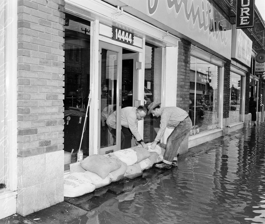 #22 Man helping a shopkeeper by putting a sand bag in front of the store, 1952.
