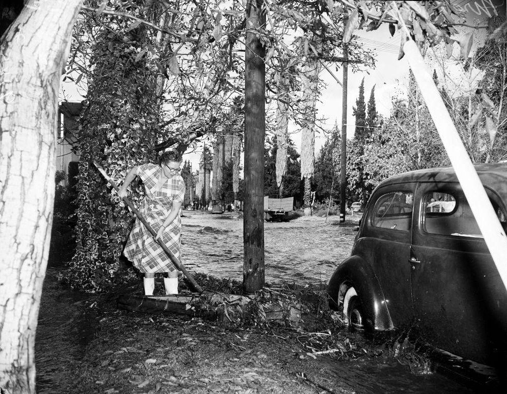 #35 Mrs Agnes Snyder removes debris from car on flooded street, Tyrone Ave. 14 November 1952