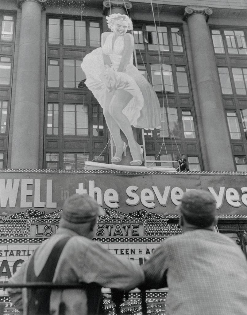 #11 Spectators gawk in Times Square as a fifty-two-foot figure of Marilyn Monroe is erected on the front of Loew’s State Theatre.