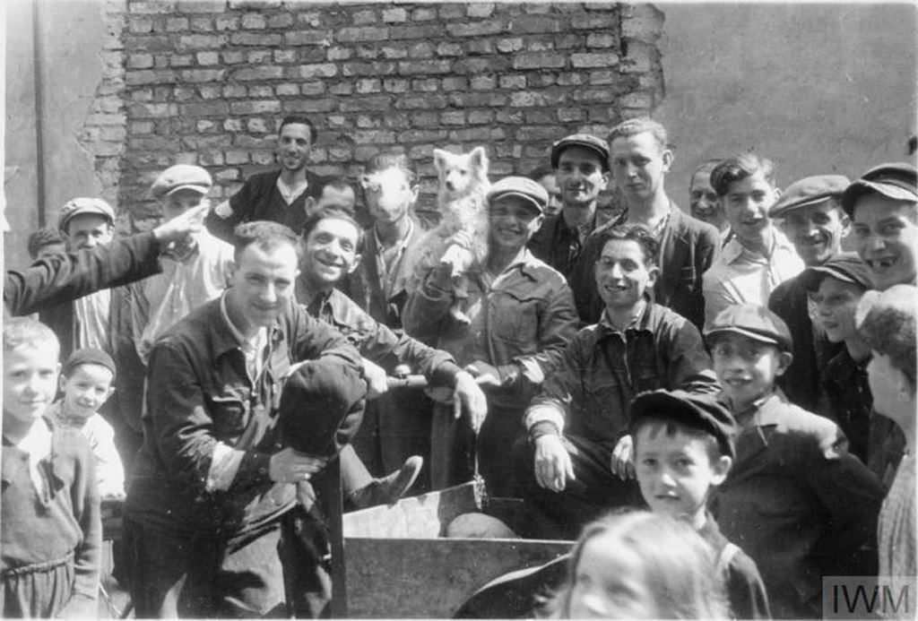 #14 A group of Jewish men and children posing for a photograph in the street of the ghetto. Note the man in the middle, holding a dog on his shoulder.