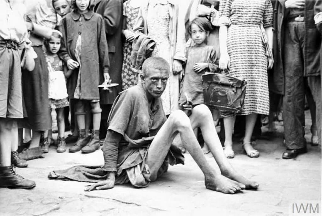 #21 An emaciated boy sitting on a pavement. Note a crowd of pedestrians around him, including children with toys.