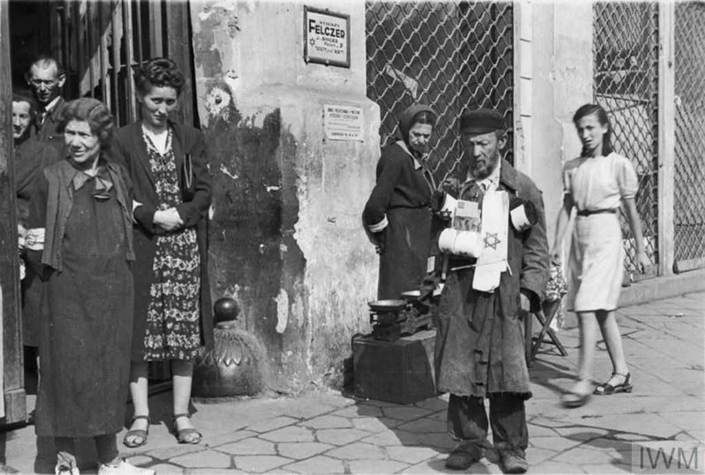 #11 A street armband seller and a group of pedestrians on 18 Zamenhofa Street (probably) in the ghetto, summer 1941. Note two advertising plaques on the wall in the background – for Senior Medic (starszy felczer) named J. Singer and for typewriting services (address given – 18 Zamenhofa Street, flat no.