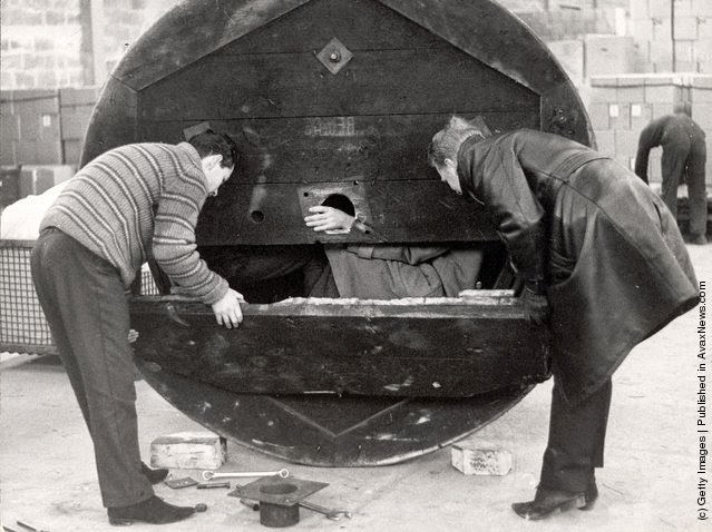 #68 Two men open a hollow metal drum used by three West German men to bring their girlfriends over the border from East Berlin, Germany, 1965.