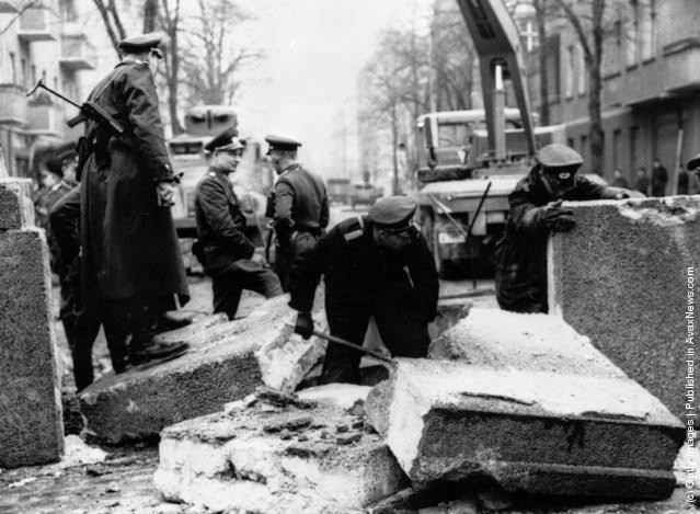 #69 Officers inspecting the damage to the Berlin Wall, East Germany, and making preparations for its repair, after an East German rammed the Wall with an army car and successfully escaped, 1963.