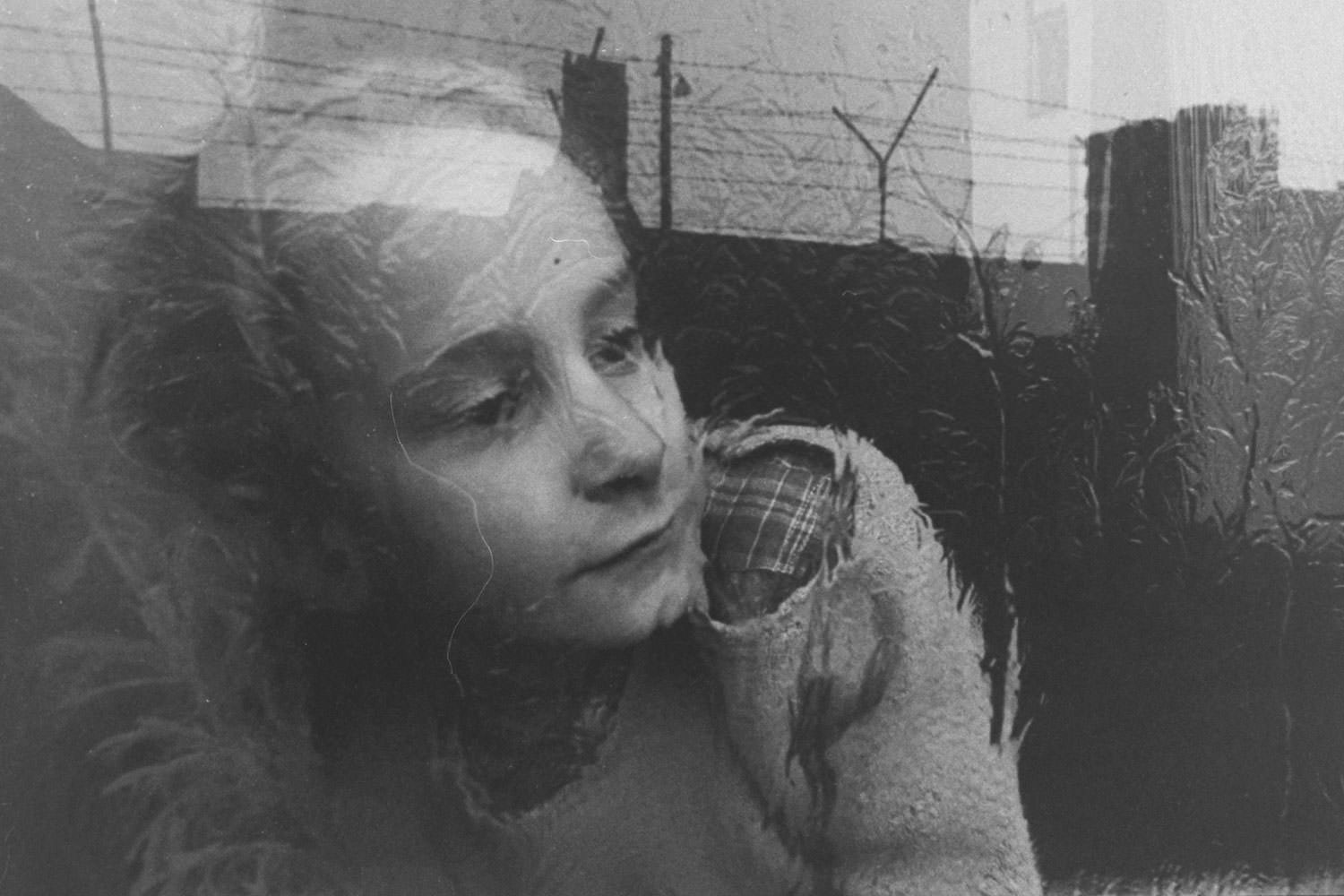 A girl looks at the Berlin Wall through a frosty window which reflects the Wall’s silhouetted barbed wire in December 1962.