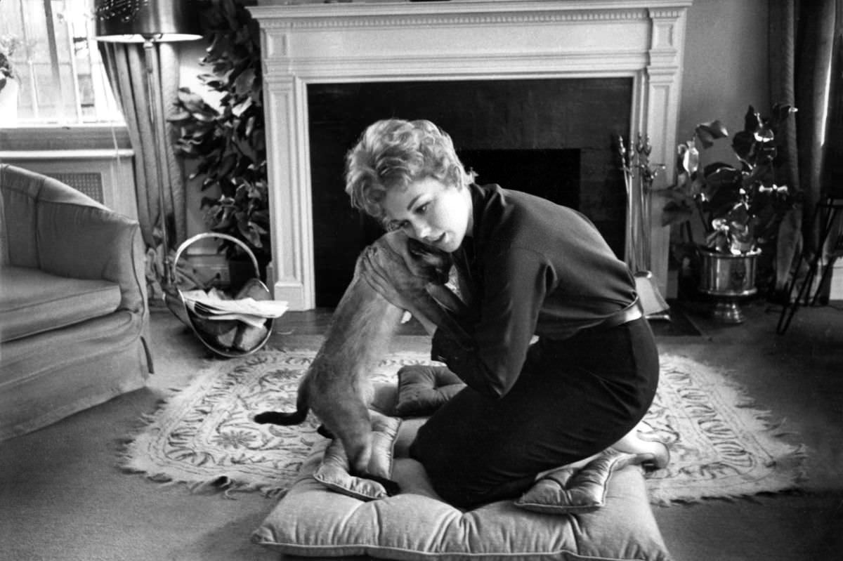 #16 Hollywood actress Kim Novak gives her Siamese a hug at home, 1959