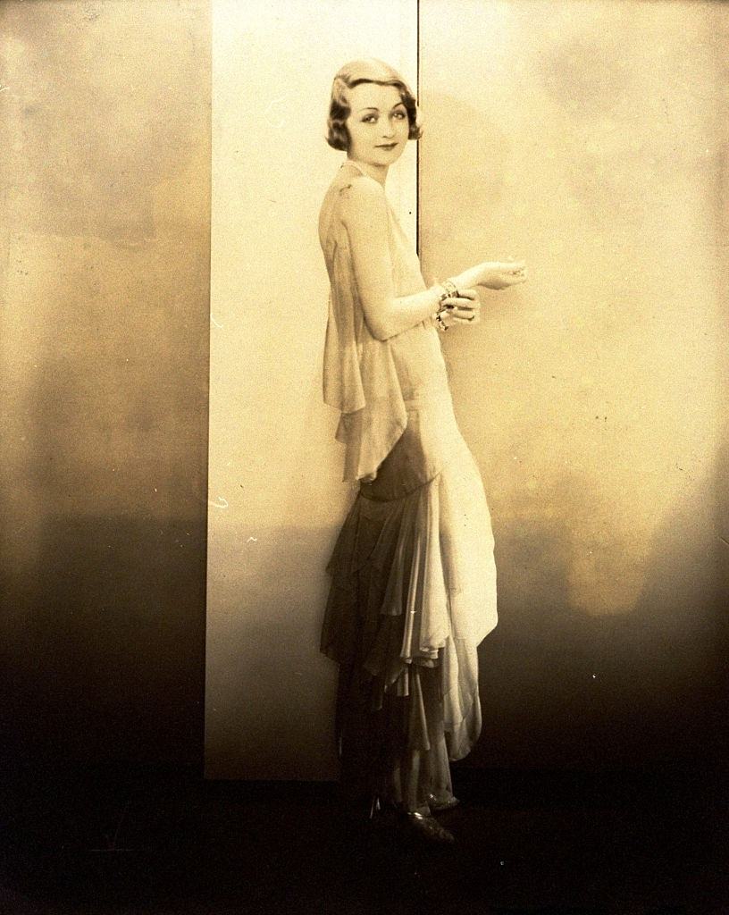 #24 Constance Bennett wearing sleeveless chiffon gown with back scarf and flounces that spiral down the skirt, Vogue 1929.