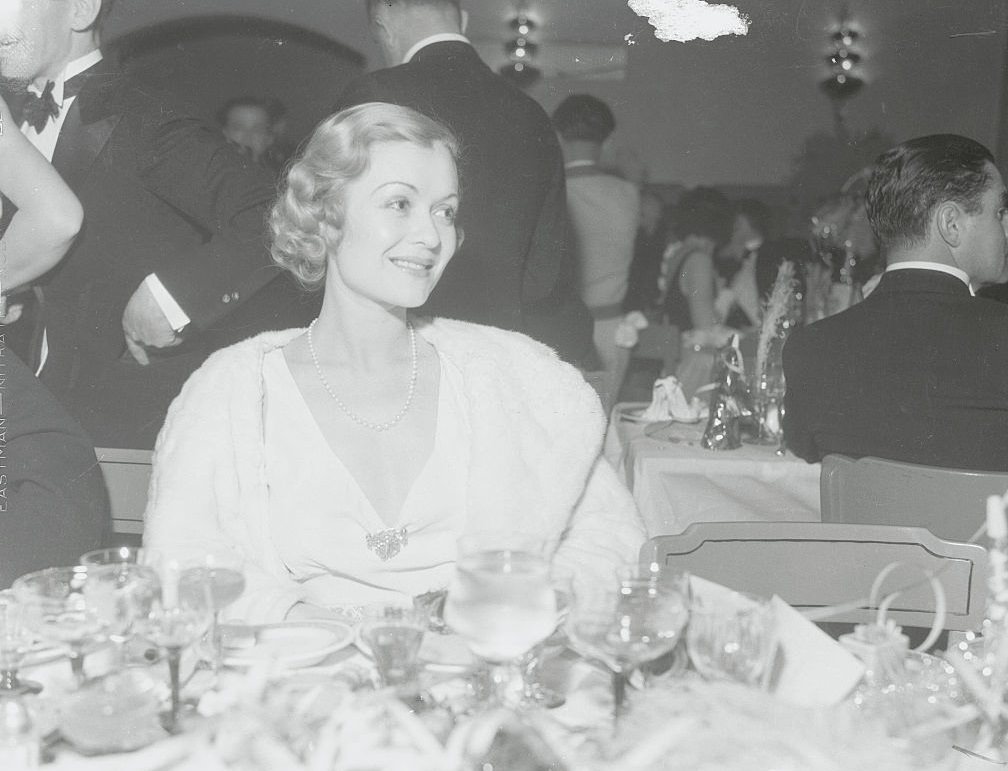 #16 Constance Bennett, smiles prettily from her table in the Agua Caliente Hotel where she celebrated New Year’s Eve with scores of members of the film colony.