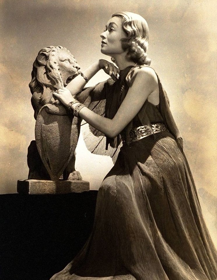 #50 Constance Bennett wearing a long gray pleated chiffon dress and cape, Vogue 1936.