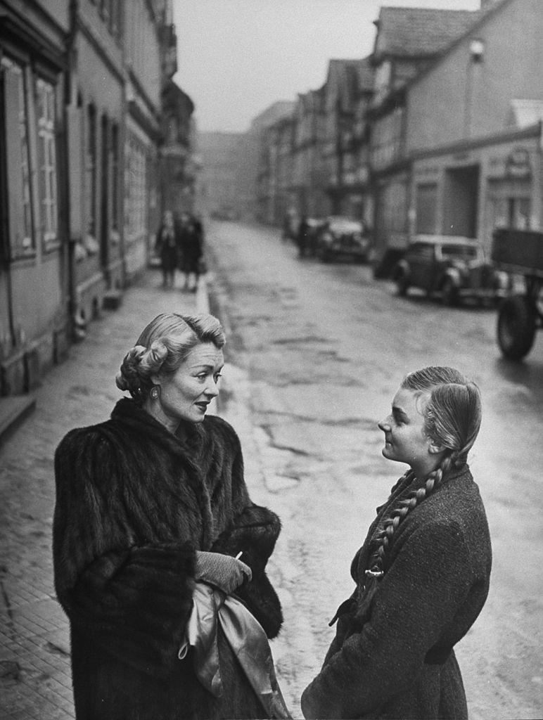 #60 Constance Bennett speaking with a young German woman, 1949.