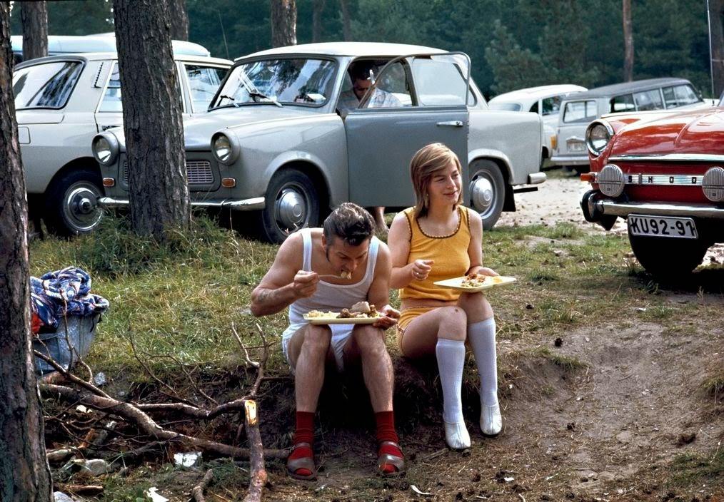 #36 Vacationers in the woods on the shore of the Baltic Sea have lunch in a parking lot in front of their Trabant and Skoda cars. Ruegen, 1974.