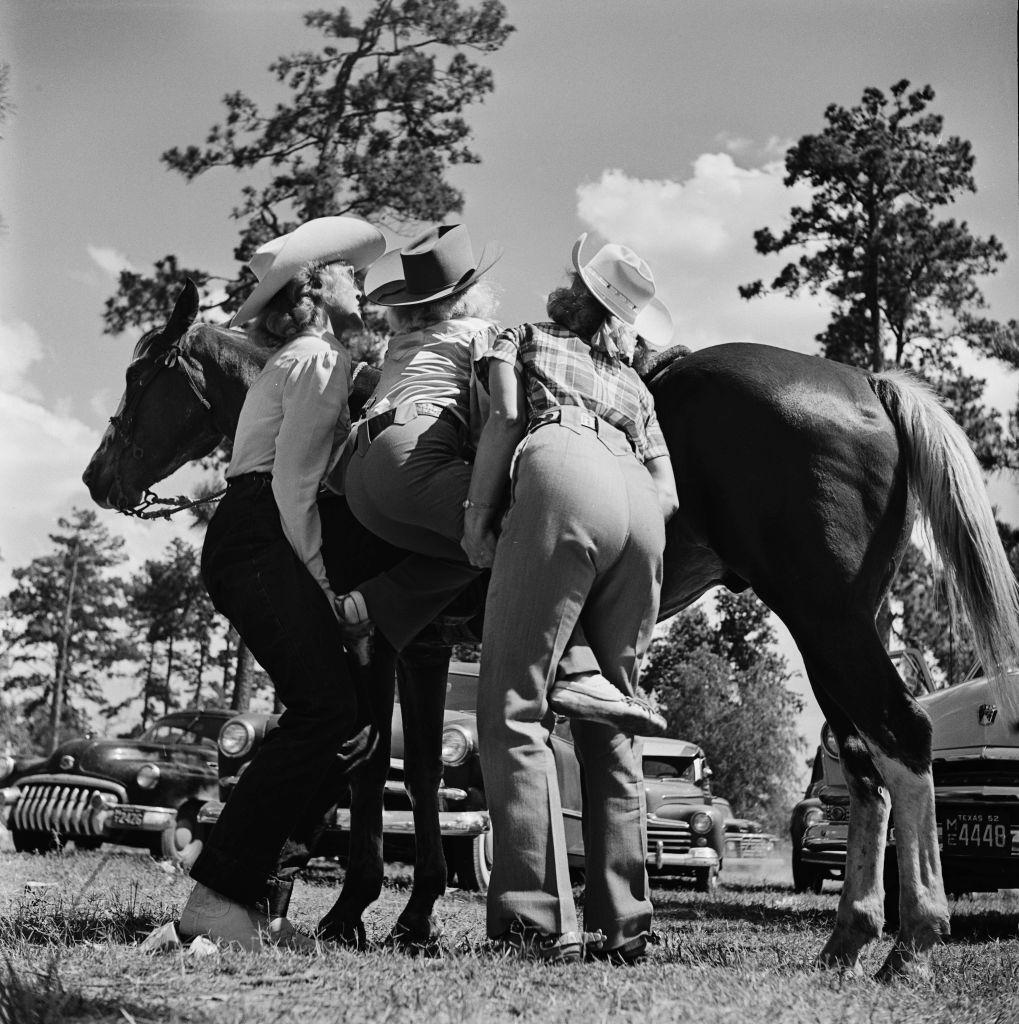 #55 Two women help a young contestant onto a horse at a youth rodeo in Houston, Texas, 29th May 1952.